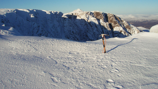 Ice axe in the foreground of a munro landscape covered in snow