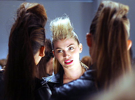 Three models with tall haircuts talk backstage at London Fashion Week. 