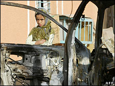 Một bé gái Iraq bên cạnh xác một chiếc xe hơi bị đốt cháy