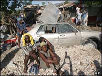 Obyvatelé města Gonaives sedí na troskách auta 