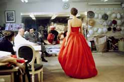 Fashion designer Christian Dior (sitting C in white coat) commenting on red gown for his new collection prior to showing. © Photo by Loomis Dean//Time Life Pictures/Getty Images.