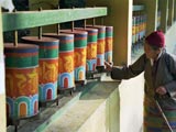 Elderly woman at a row of wooden, brightly painted prayer wheels