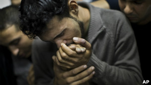 Palestino beija a mão de parente morto em ataques, em Gaza, neste domingo (AP)