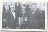 Dafydd Morris o gwmni Brodyr Hogan yn cyflwyno ffeil i Gwyn Hefin Jones, cadeirydd y côr