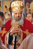 Coptic Orthodox Pope Shenouda III, bearded gentleman with cane in red and gold robe and headdress adorned with equal-armed Christian crosses