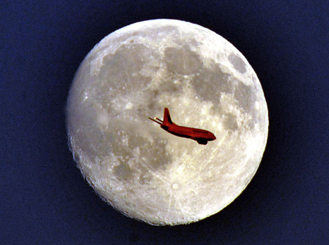 A plane passes over the face of the full moon