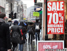 People passing sale signs in shop windows