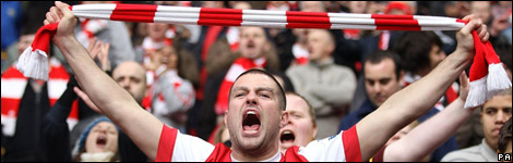Arsenal fan at a match, holding up a scarf up and shouting 