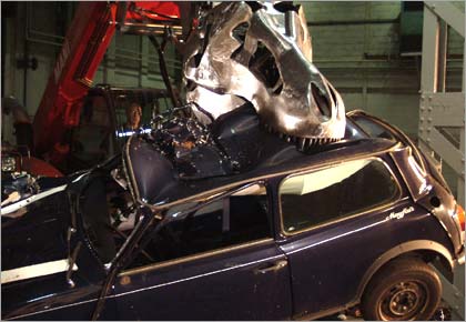 A steel replica T. rex head takes a bite out of a small car.