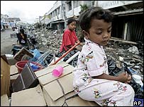 Menina espera enquanto os pais recolhem produtos da loja da família, destruída pelo tsunami