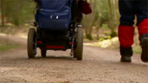 Wheelchair and a walker's feet heading down a forest path