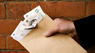 A hand offers a brown envelope bursting with banknotes