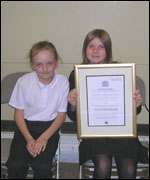 Two schoolchildren hold a framed award