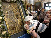 Matka s dítětem líbá ikonu