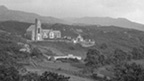 Black and white view of a tall, Gothic-style church set among hills with trees, grass and heather.