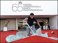 Работник го подготвува црвениот килим пред влезот на филмската палата