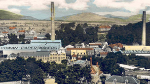 Black and white view of Penicuik, a wide, unsurfaced road lined by two and three-storey buildings with ground floor shops.