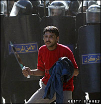 يکی از هوداران دولتی که مسلح به چاقو است در برابر پليس ضدشورش ايستاده است