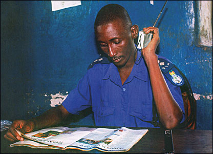 A policeman reads a magazine while holding a transistor radio to his ear