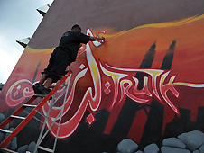 Man on ladder working on orange-brown wall with Arabic inscription
