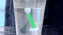A piece of straw with sticky-tack floats to the top of a cup of water