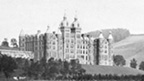 Black and white view of a large, five-storey hotel set on a wooded hillside above fields. The stone building is in Renaissance style, with a symmetrical frontage and a roofline featuring several turrets. A long conservatory extends from one side of the building.