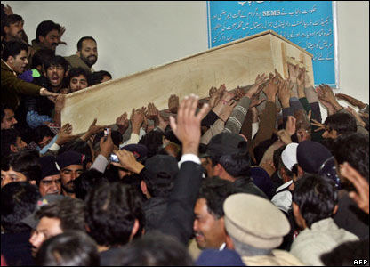 Njerëzit e tronditur duke transportuar arkivolin e thjeshtë prej druri që barte trupin e pajetë të zonjës Bhutto.