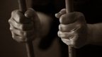 Image of hands holding prison cell bars