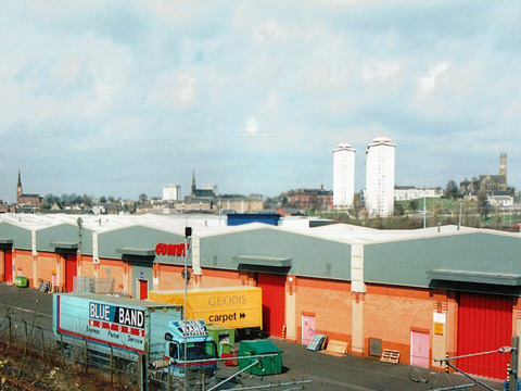 Colour view of the back of a row of modern retail outlets with the skyline of Coatbridge behind.