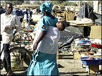 A woman with a child on her back walks through a market in a southern Algerian town
