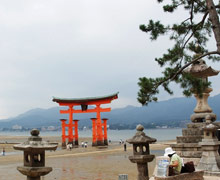 Itsukushima's red arch at low tide, standing on the sand of Miyajima beach, with people walking around the base