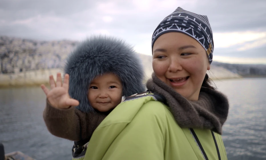 A mother with a baby on her back, both smiling.